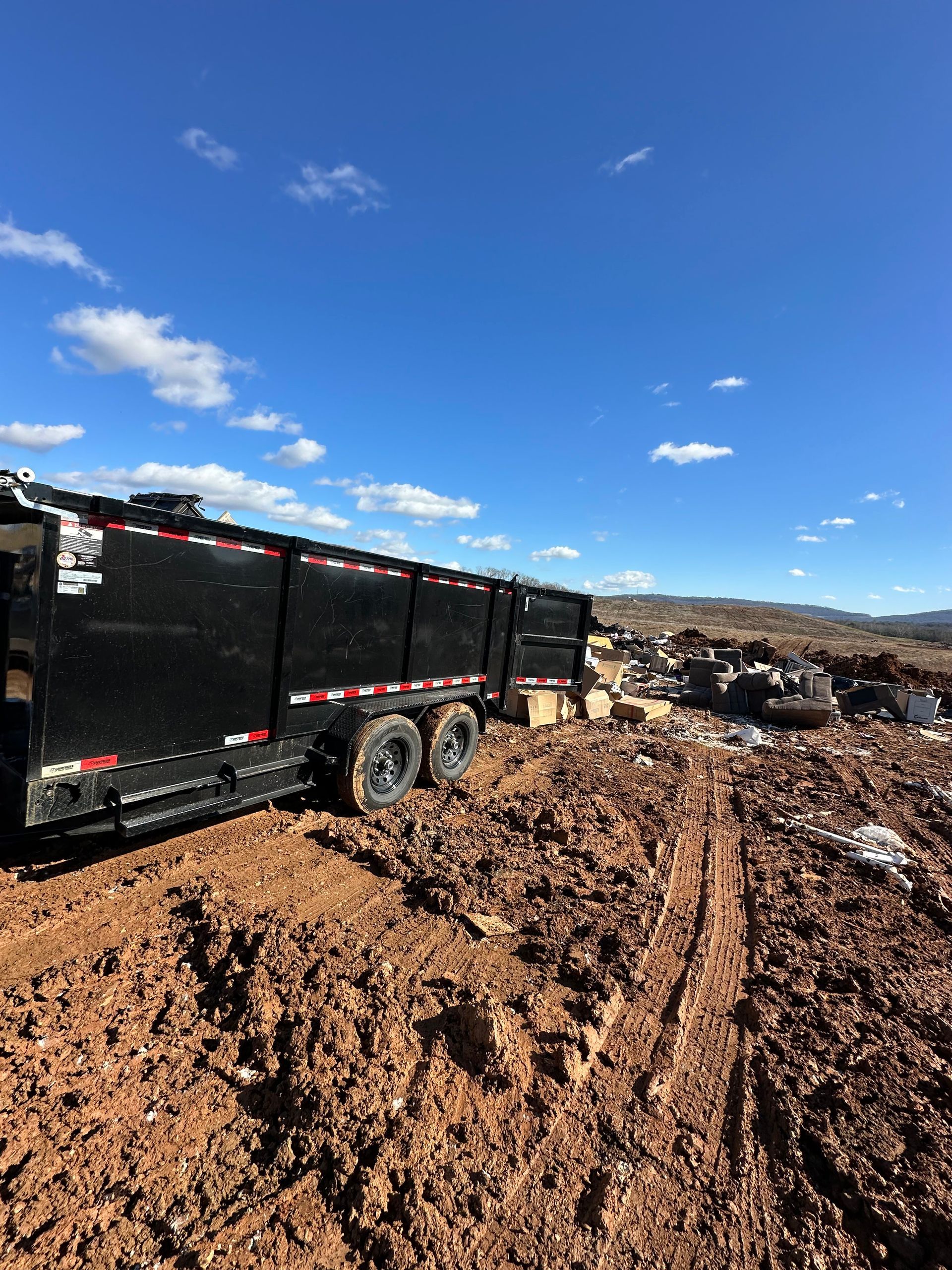 Black dump trailer on muddy ground under a blue sky.