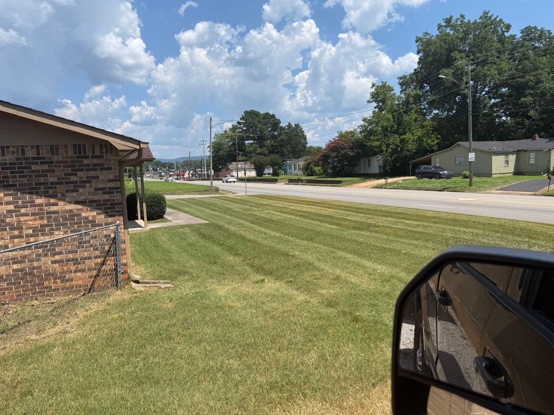 Lawn mowed with striping, street in front of houses, sunny day, part of car mirror.