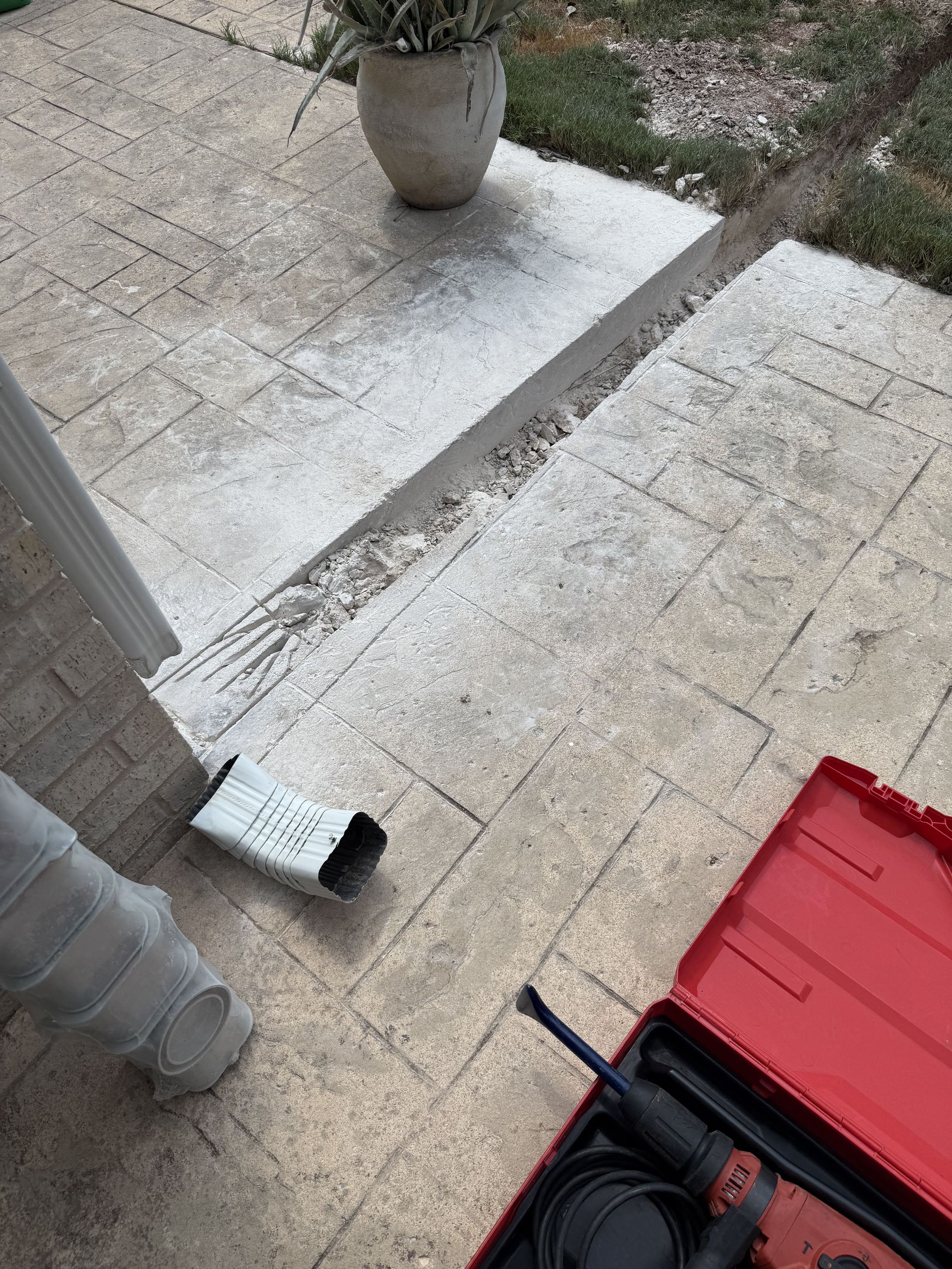 A broken sidewalk with a gutter's downspout and a toolbox present.