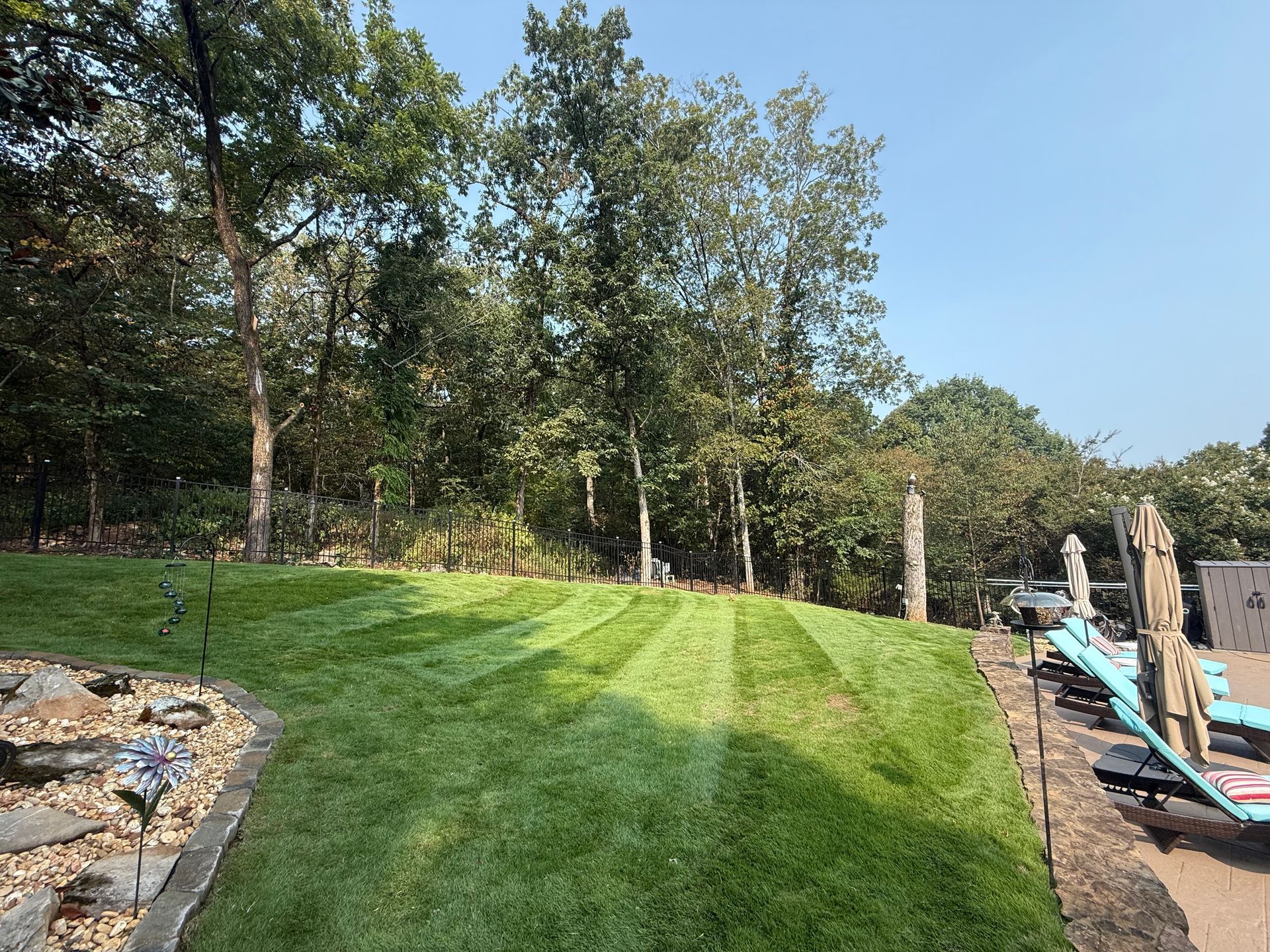 Lush green lawn with mowed stripes, leading to a wooded area. A pool is visible on the right side.