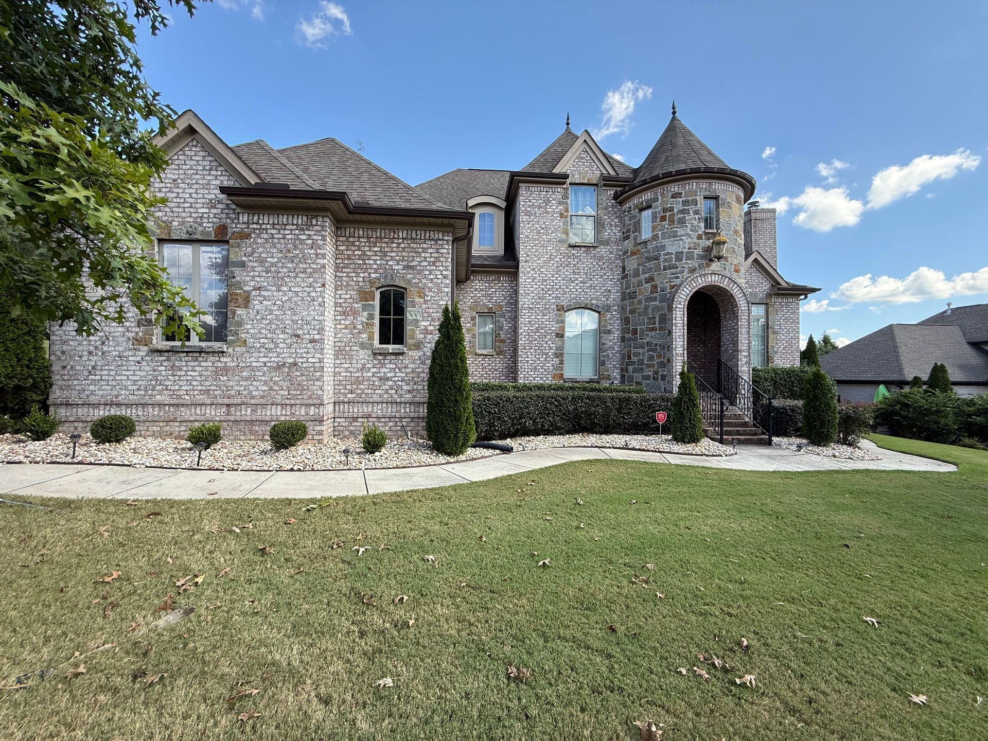 Brick house with a turret, arched doorway, and manicured lawn on a sunny day.