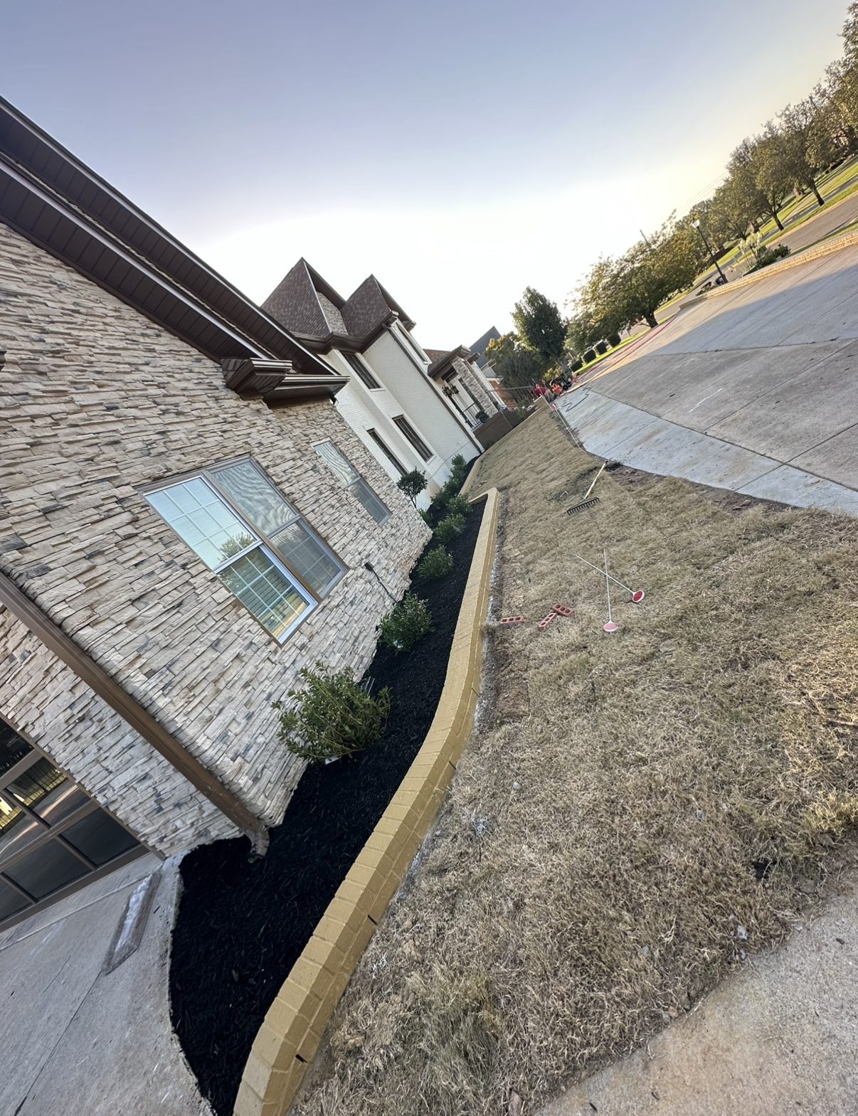 House with stone exterior, landscaped bed with dark mulch, and driveway angled upward.