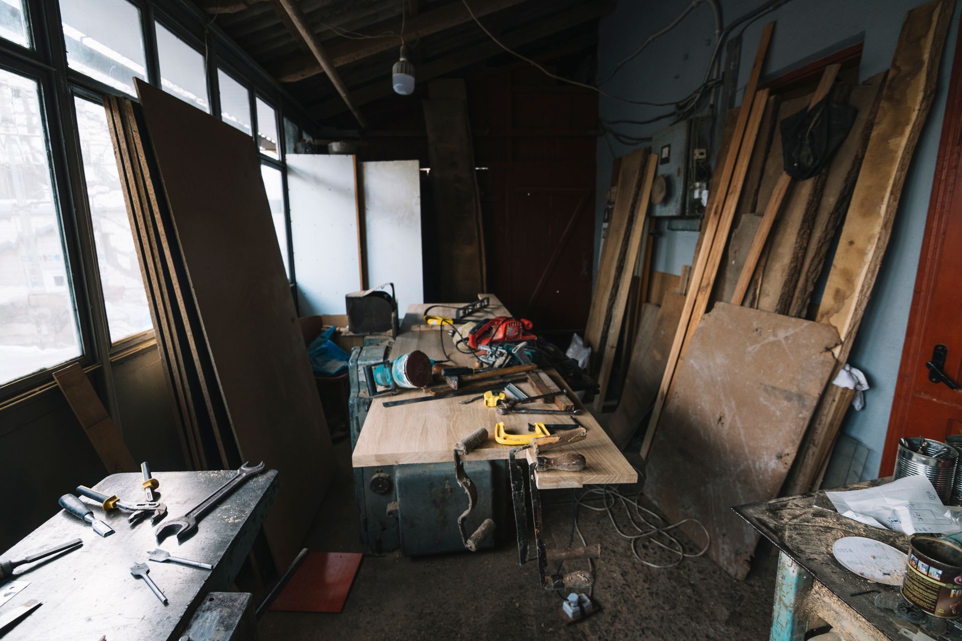Workshop interior with cluttered workbench, tools, lumber, and wood panels.