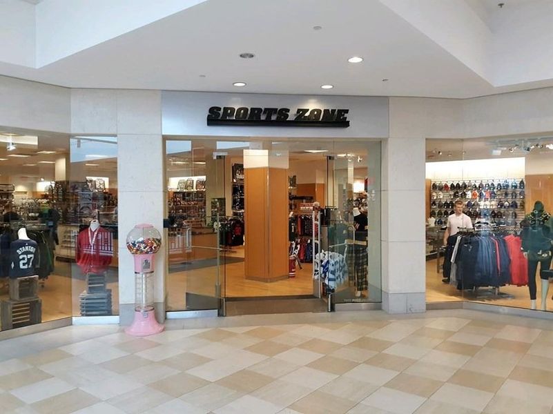 Sports Zone store entrance in a mall, with glass doors and windows, displaying merchandise.