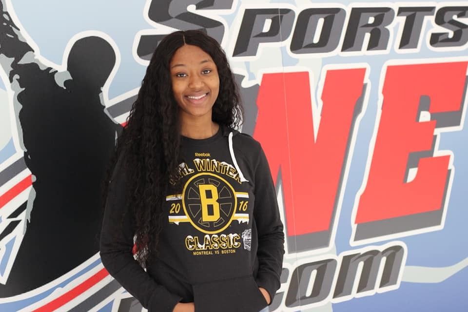 Young Black woman smiling, wearing a black sweatshirt with a gold 
