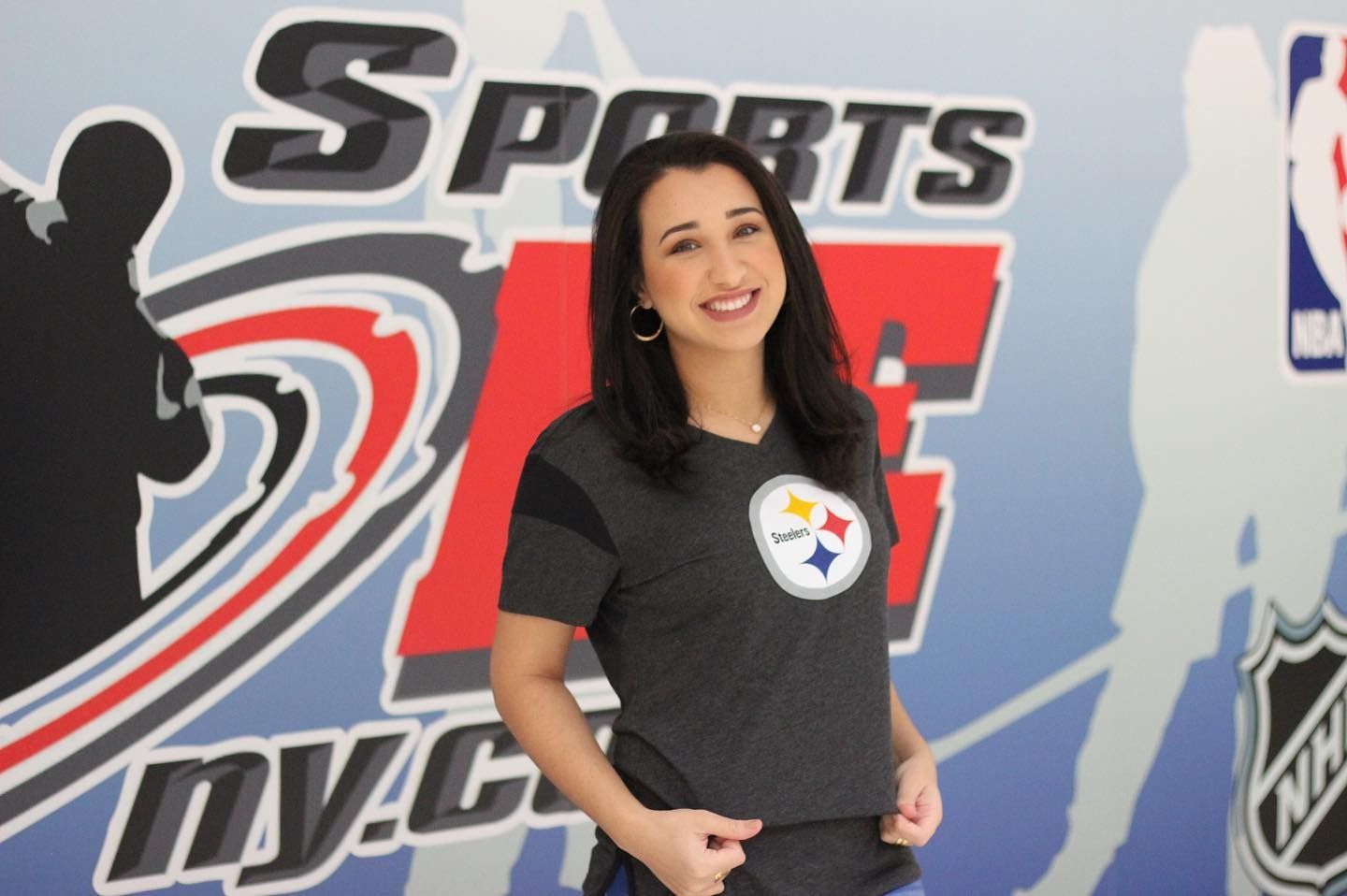 Woman smiling, wearing a Pittsburgh Steelers t-shirt in front of a sports-themed backdrop.