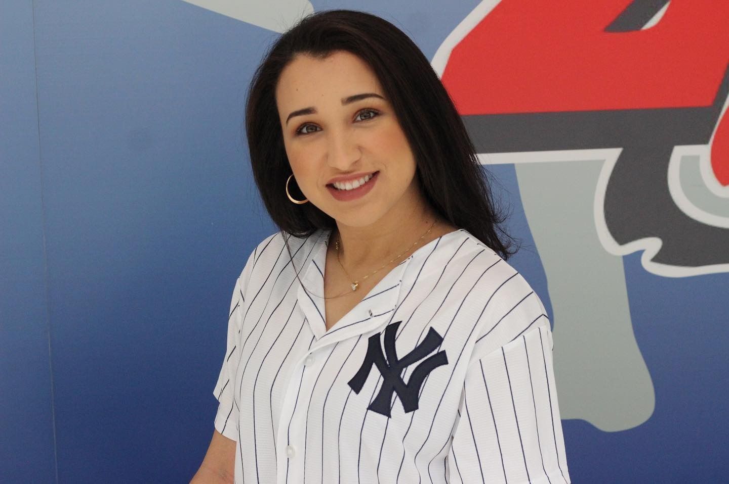 Woman in Yankees jersey smiles in front of a blue and red logo.