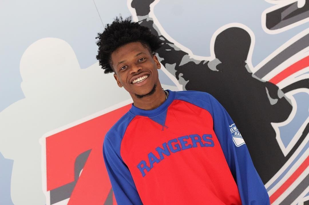 Man wearing a red and blue Rangers shirt smiling, against a stylized background with the word 