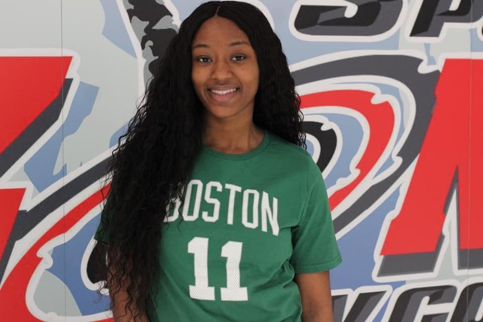Woman with long black hair, smiling, wearing a green Boston Celtics shirt with 