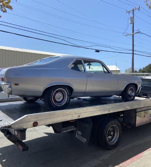 Silver classic car on a tow truck, outdoors on a sunny day.