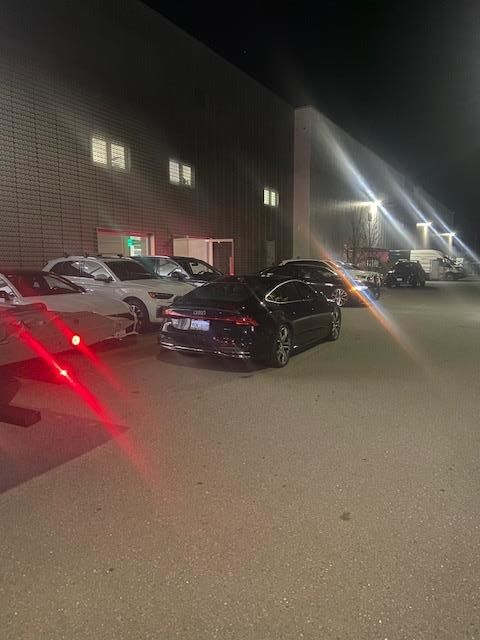 Cars parked outside a building at night. Dark sedan in the foreground, other cars visible. Lights.