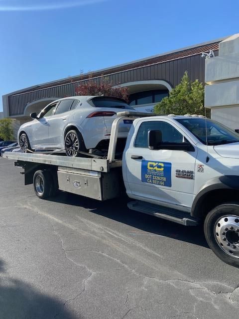 White SUV being towed on a flatbed tow truck, parked on pavement in front of a building.