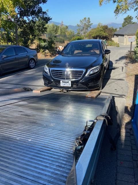 Black Mercedes-Benz sedan on a tow truck bed, outdoors on a sunny day.