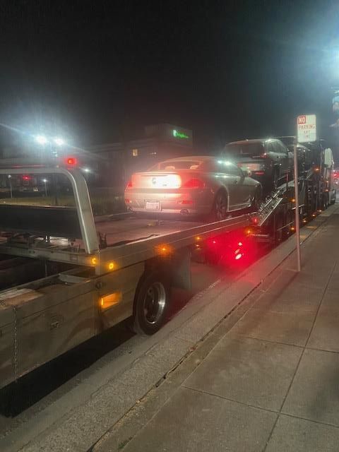 A car being transported at night on a tow truck, with red lights flashing.