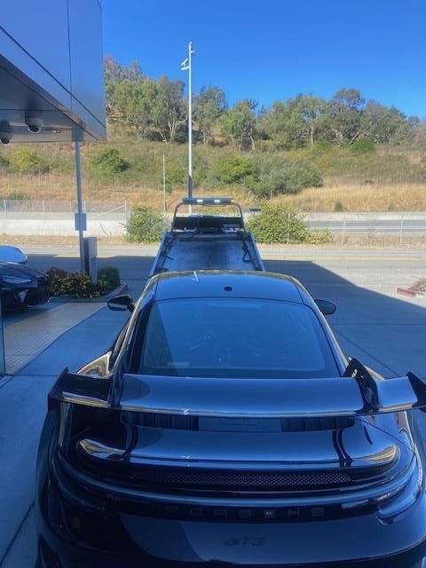 A dark Porsche sports car on a tow truck at a dealership.