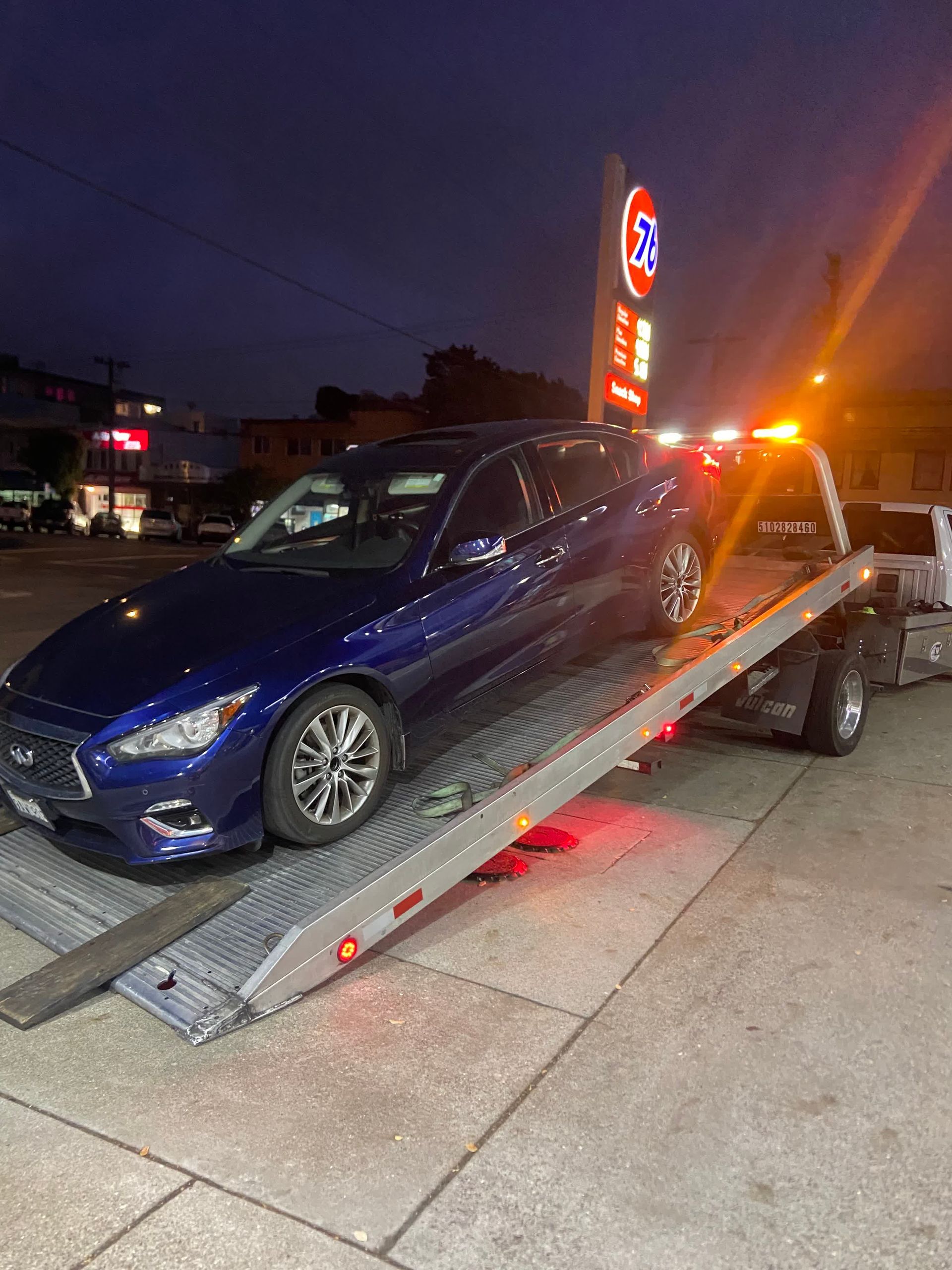 Blue car on a tow truck at a gas station, night time.