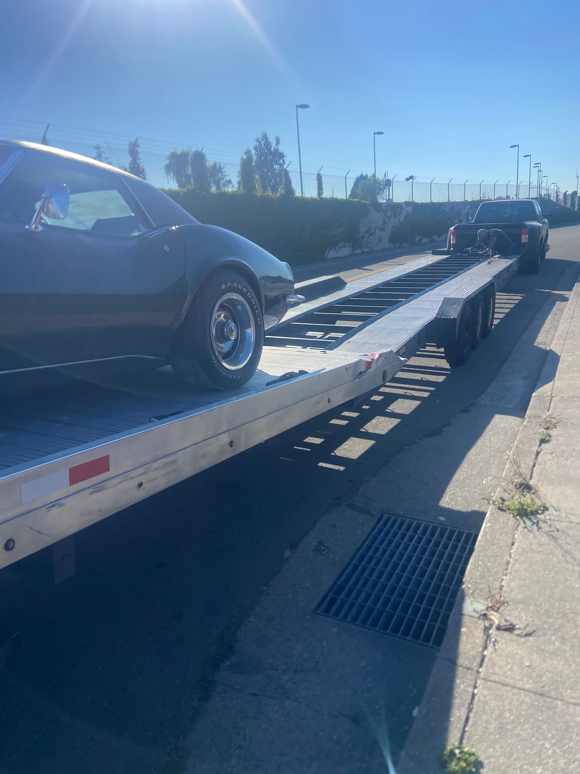 A dark car on a silver flatbed trailer on a sunny day.