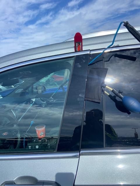 Car window with black trim being worked on, with a tool and can.