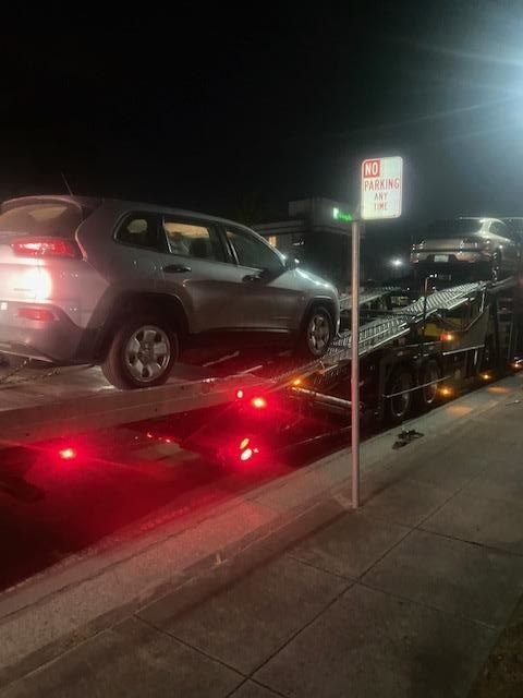 Silver SUV being towed at night next to a no parking sign. Red lights are illuminated.