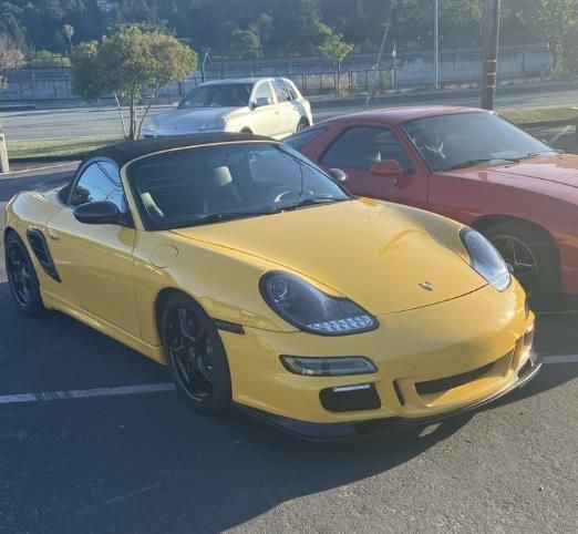 Yellow Porsche Boxster convertible parked next to a red car in a parking lot.