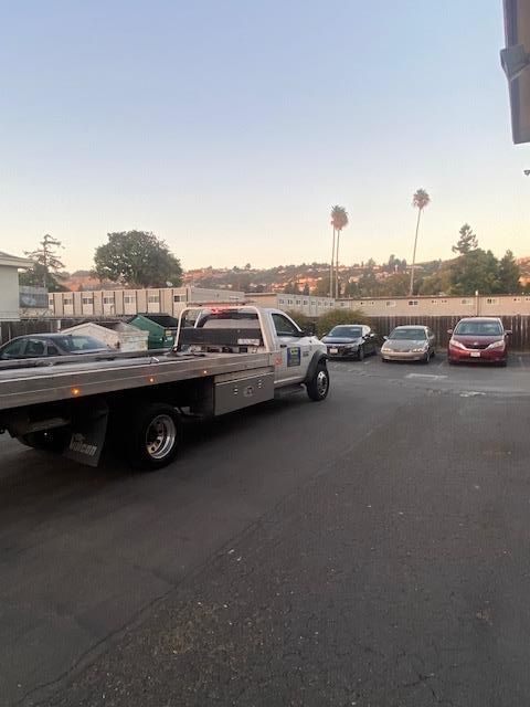Tow truck parked next to several cars in a parking lot.