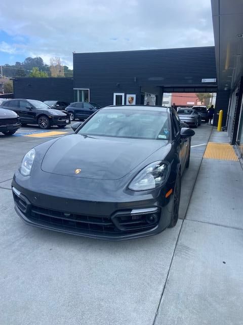 Dark gray Porsche Panamera at a drive-thru window, with other cars and building in the background.