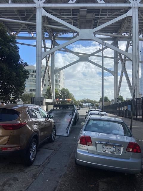 Tow truck loading a silver car under a bridge on a sunny day.