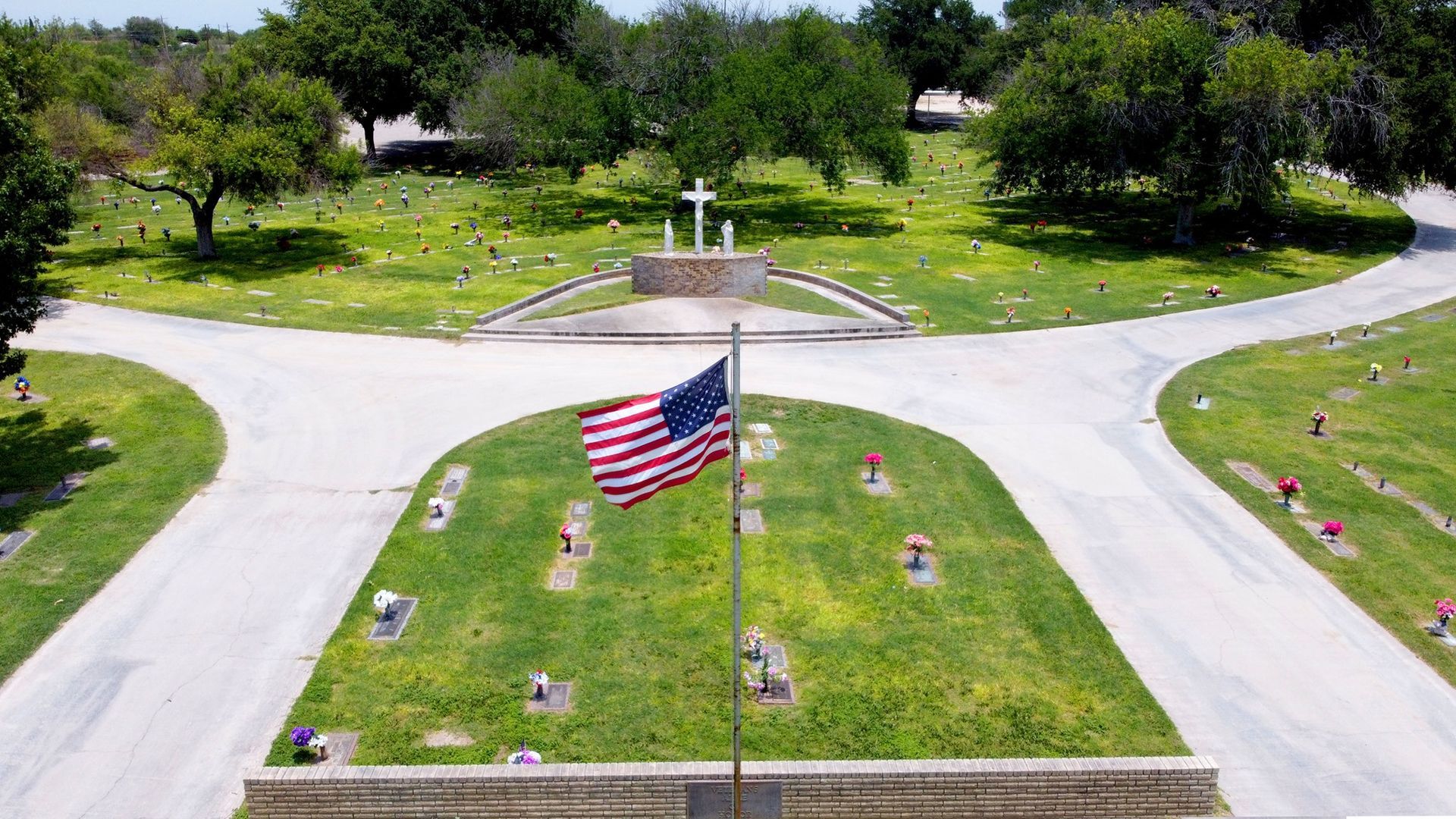 Aerial view of a memorial plaza with an American flag, curved roads, and trees surrounding it