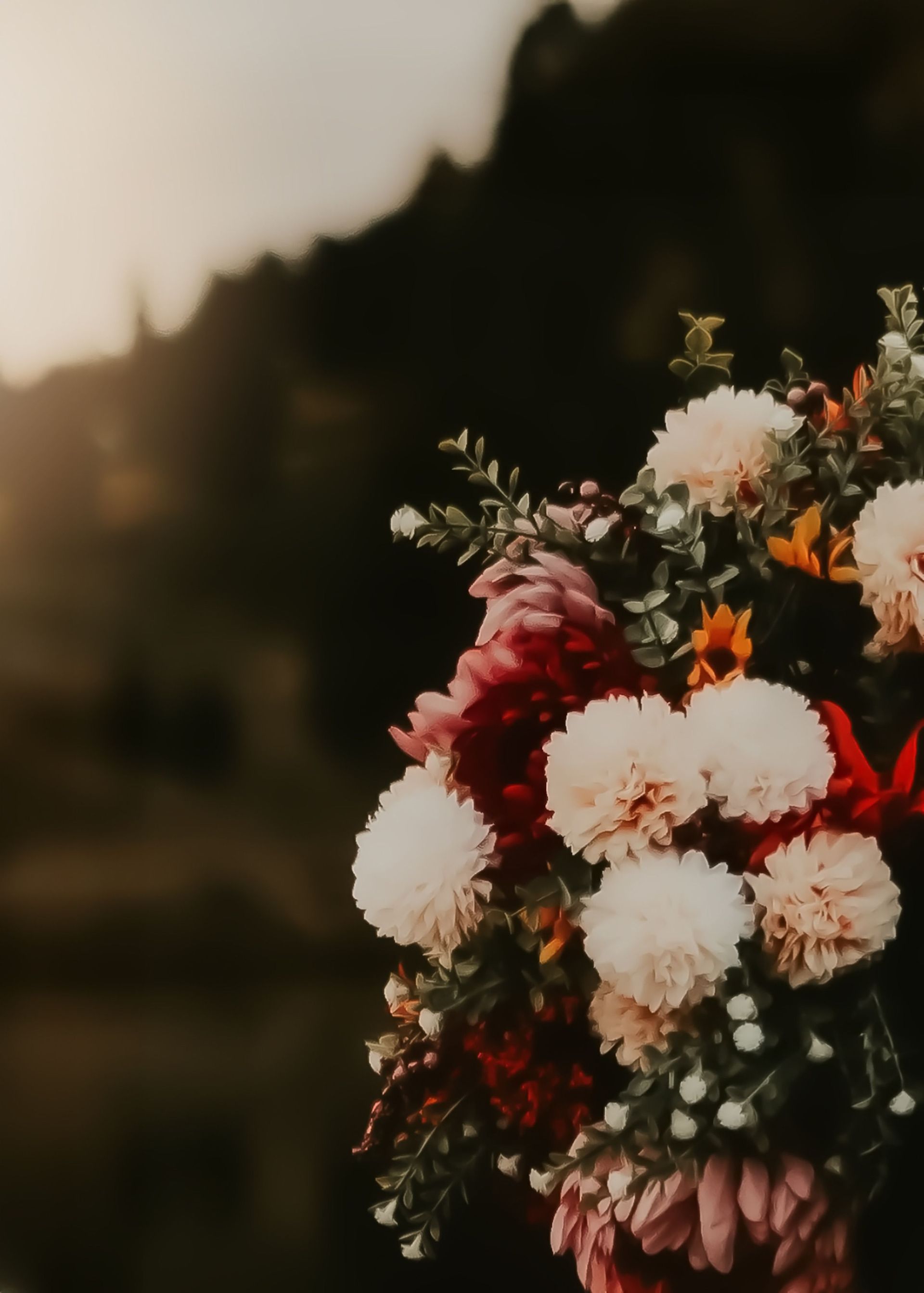 A bouquet of white, pink, and orange flowers against a blurred sunset background.