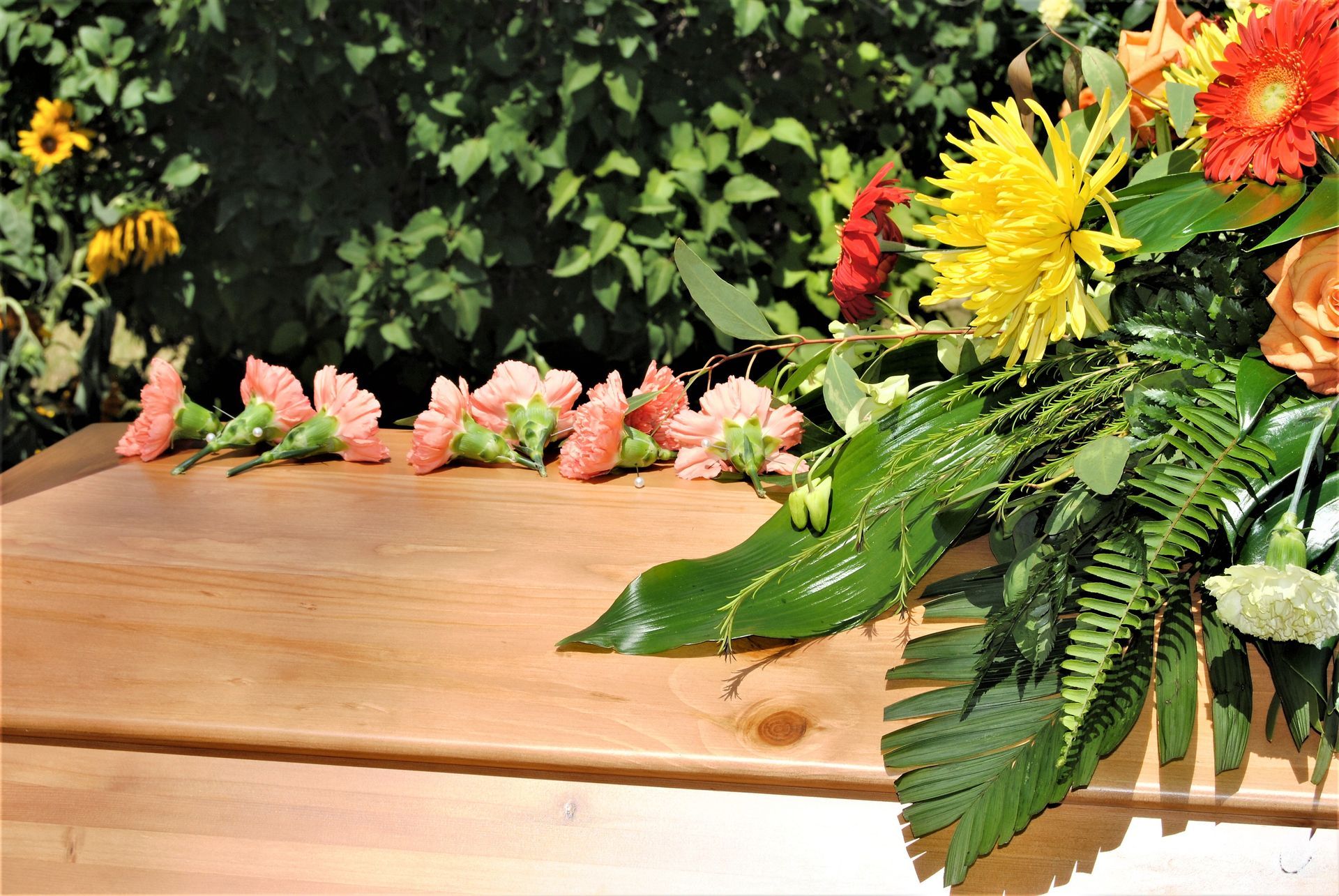 Flower arrangement on a wooden table with pink, yellow, and orange blossoms against green foliage.