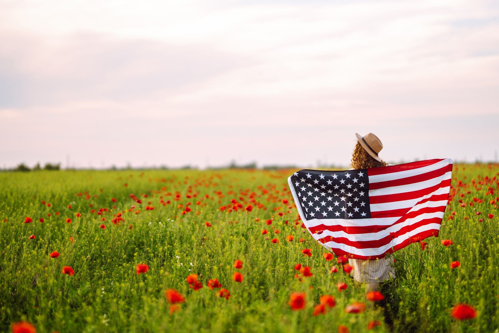 Person holding a U.S. flag in a red flower field at sunset