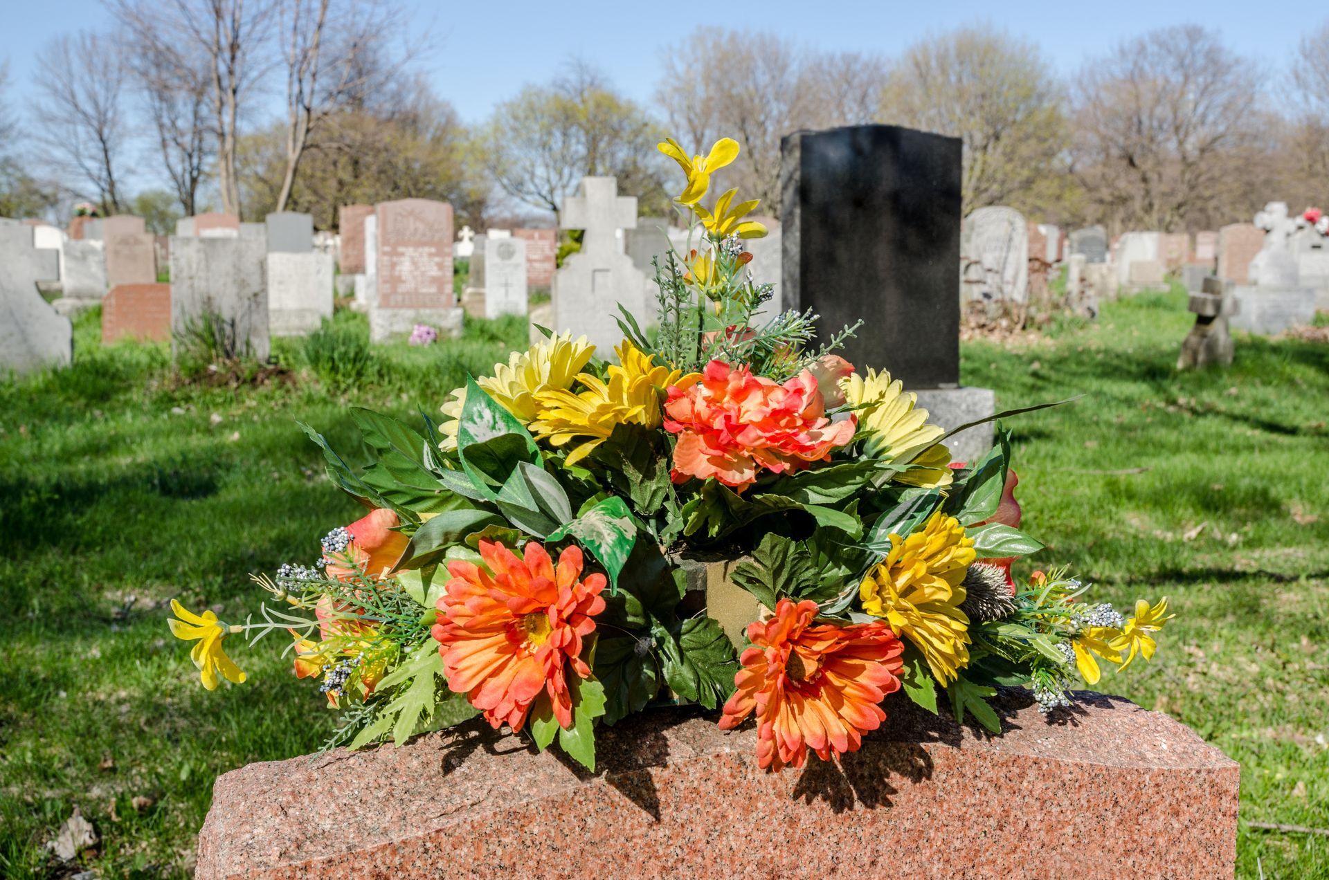 Flower arrangement on a gravestone in a cemetery, with headstones and trees in the background.