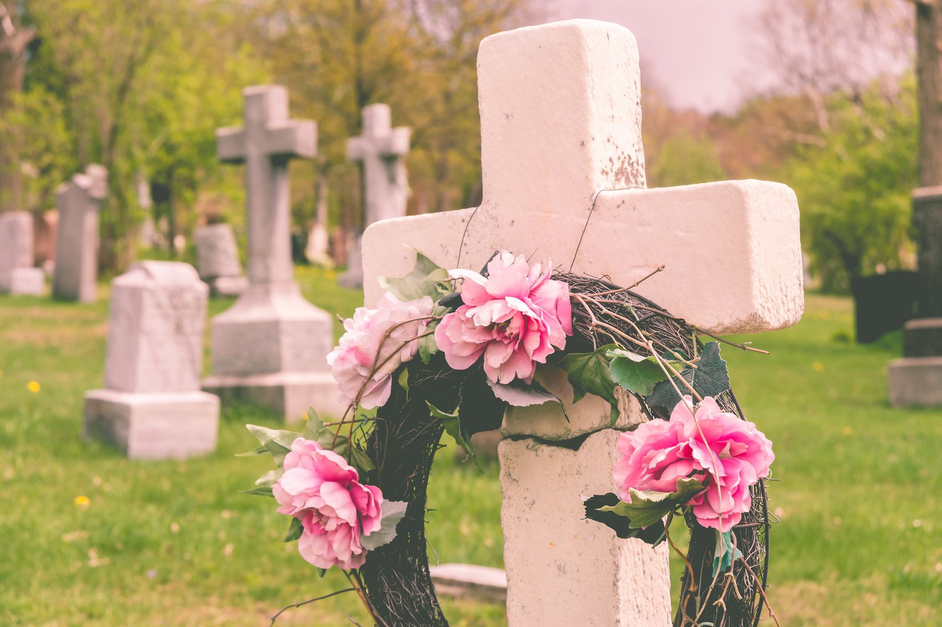 White cross gravestone adorned with pink flowers in a cemetery