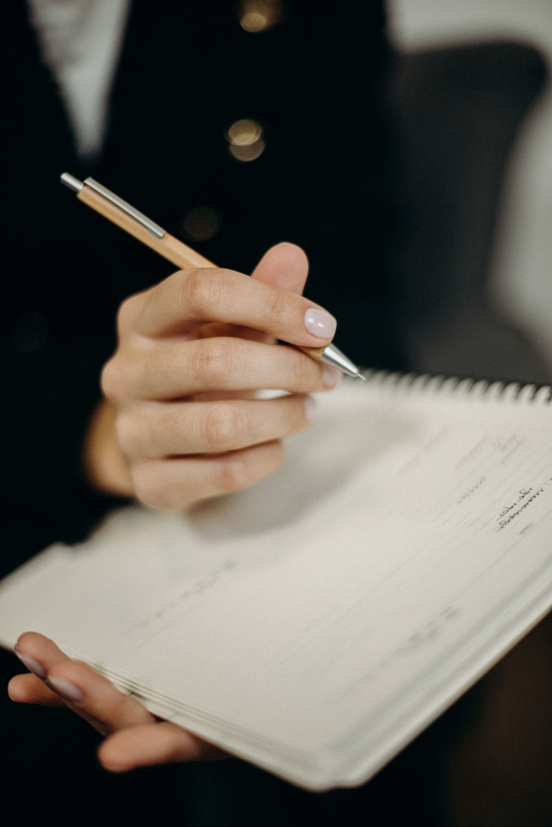 A woman is holding a pen and writing in a notebook.
