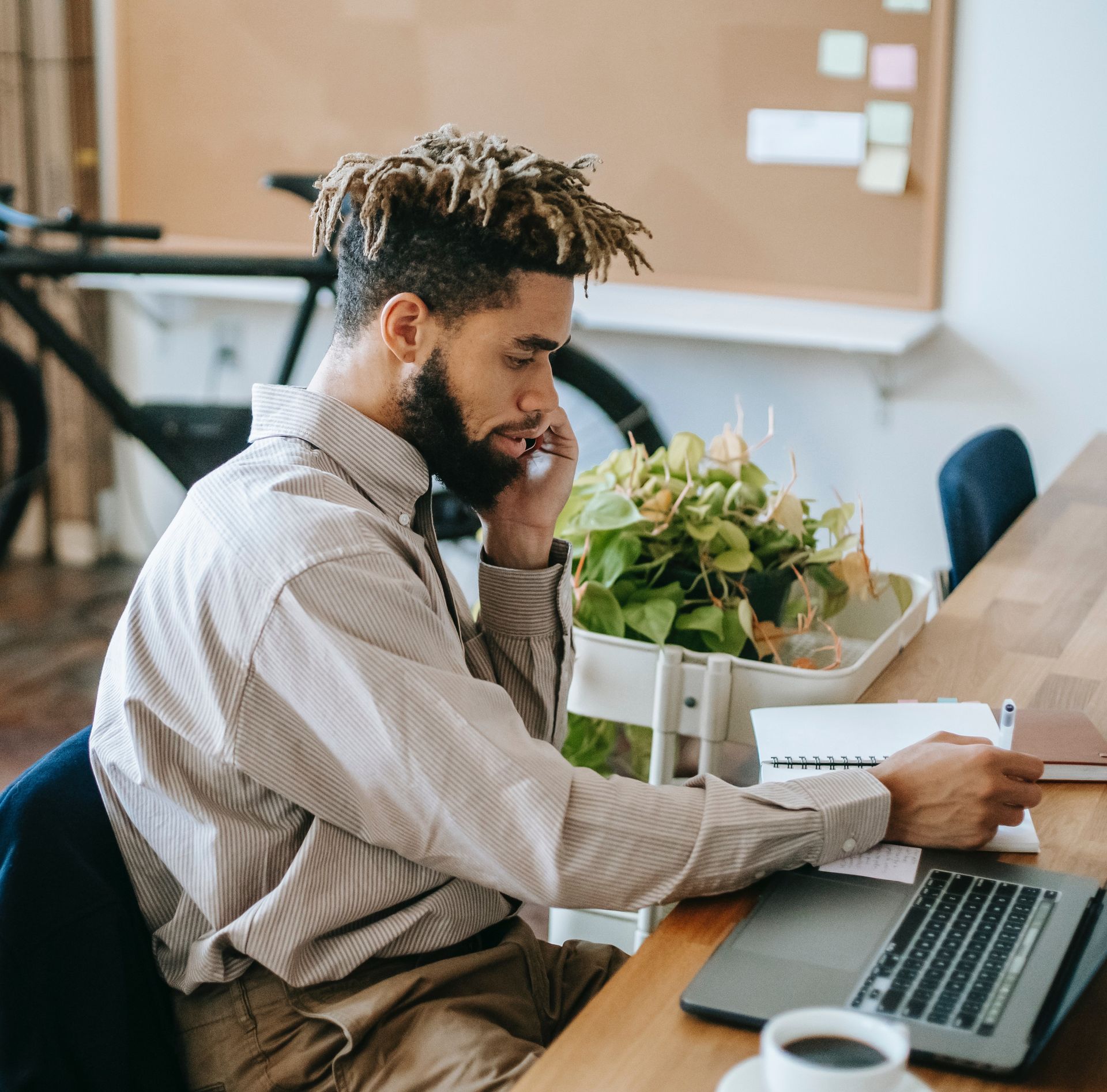 A man is sitting at a desk with a laptop and talking on a cell phone.