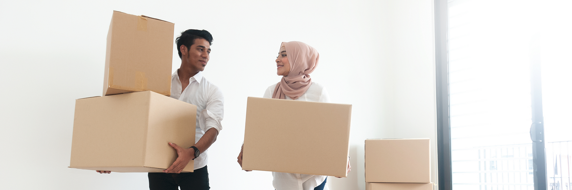 A man and a woman are carrying cardboard boxes into a new home.