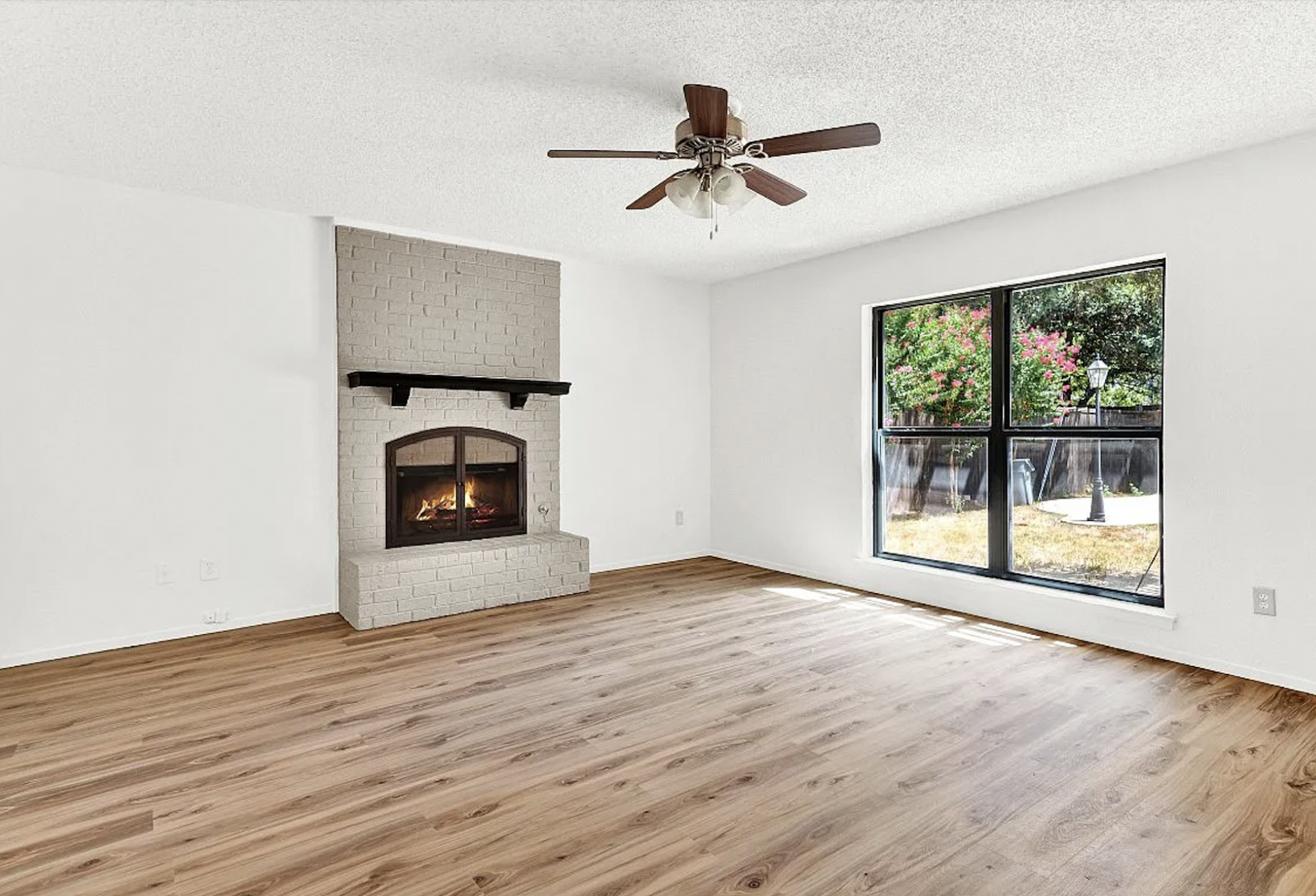 An empty living room with a fireplace and ceiling fan.