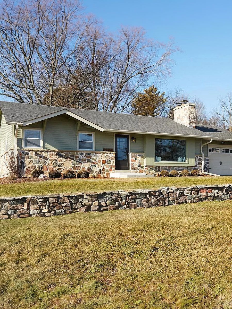 A house with a stone wall in front of it is sitting on top of a lush green field.