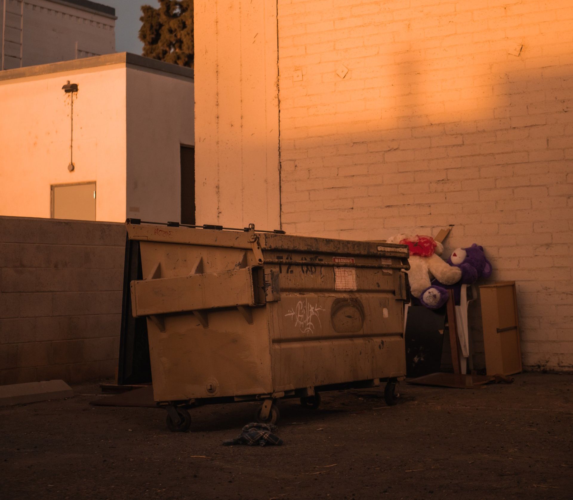 a dumpster filled with stuffed animals sits in front of a brick wall .