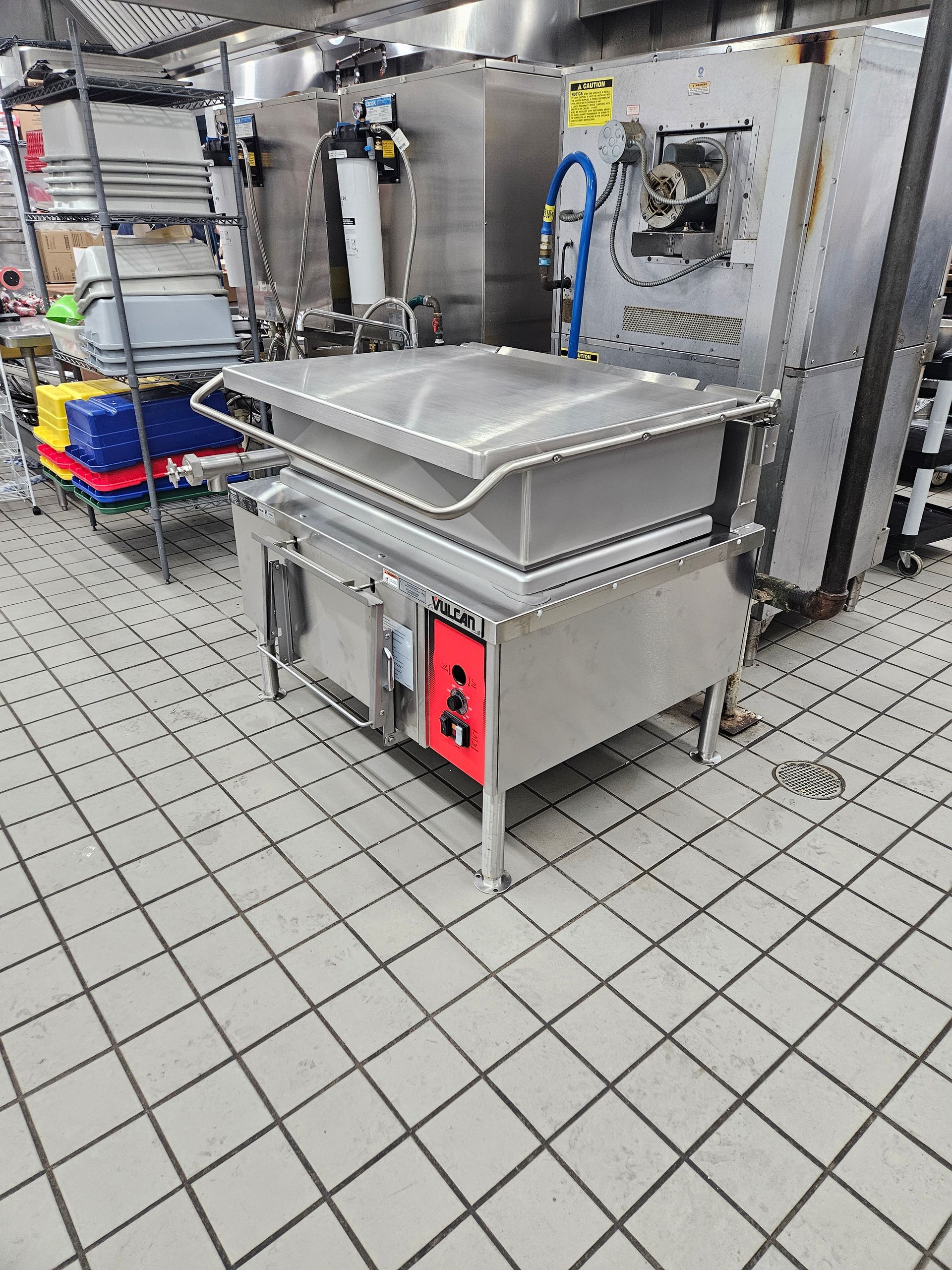 Stainless steel industrial tilt skillet in a commercial kitchen. Red control panel. Tile floor.
