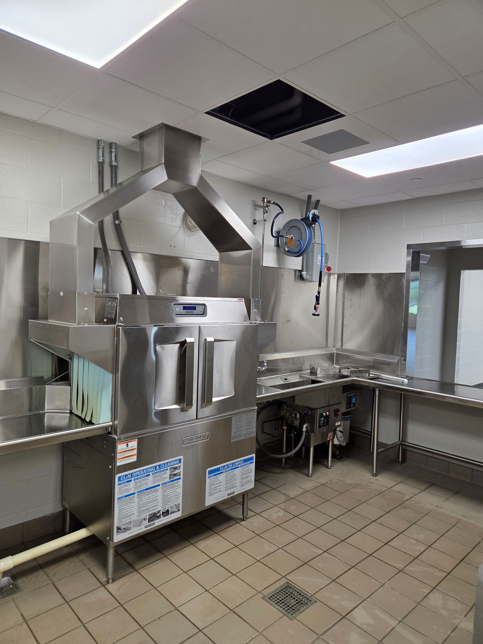 Commercial kitchen with large stainless steel dishwasher, ventilation hood, and adjacent work surfaces.