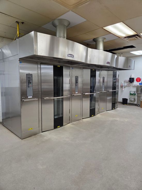 Person in work clothes opening a large stainless steel refrigerator in a commercial kitchen.