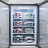 A commercial refrigerator with open doors displaying many containers of various foods, neatly organized on shelves.