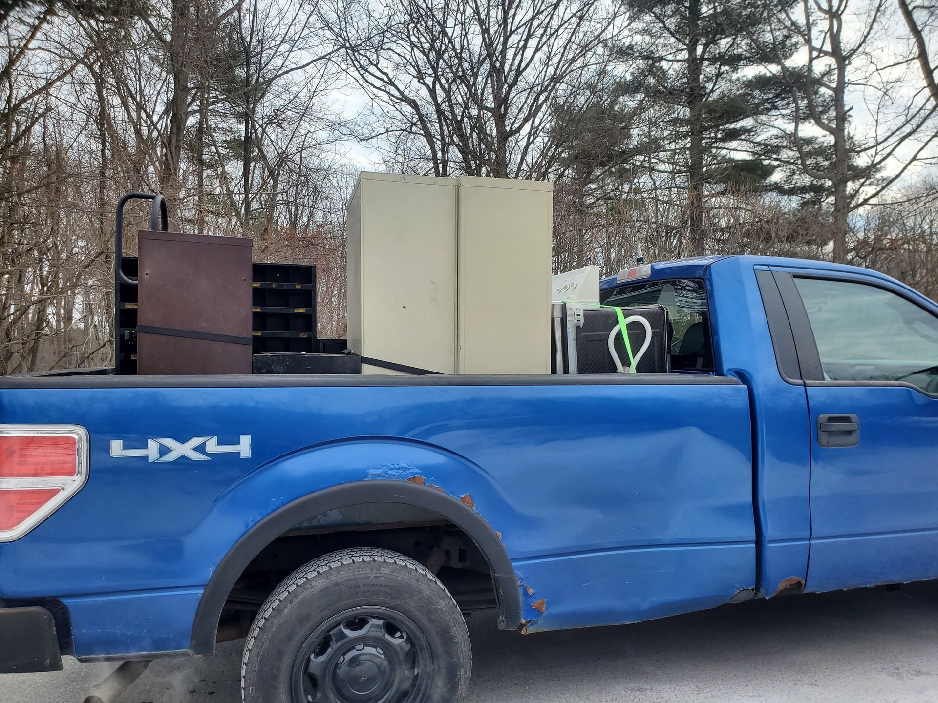 Blue pickup truck loaded with items, including a large beige cabinet.