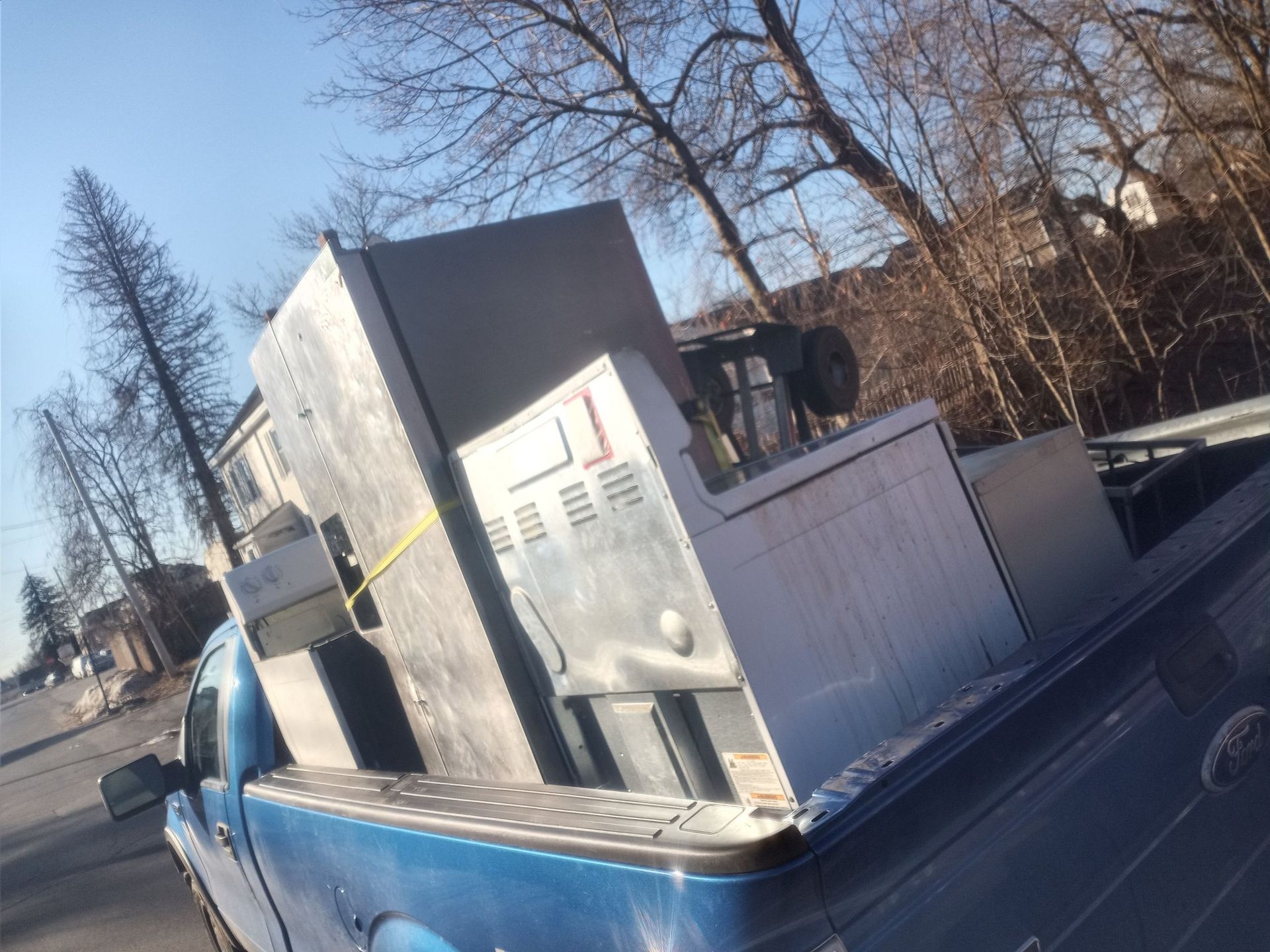 A blue pickup truck bed loaded with large, metal appliances, possibly for recycling.