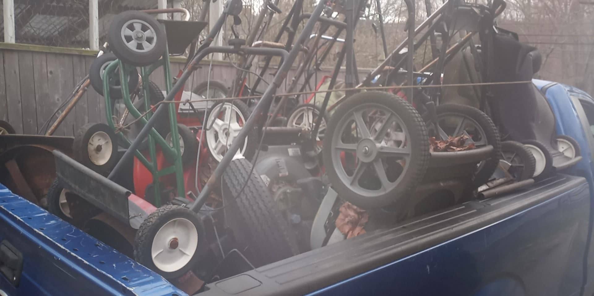 A blue pickup truck bed filled with several lawnmowers.