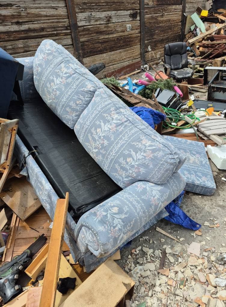 A discarded blue floral recliner sofa in a debris pile.