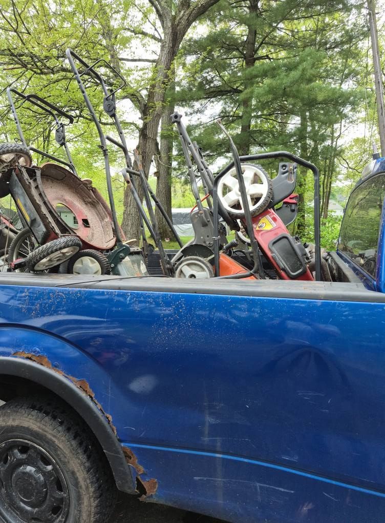 Blue pickup truck bed filled with multiple lawnmowers, outdoors.
