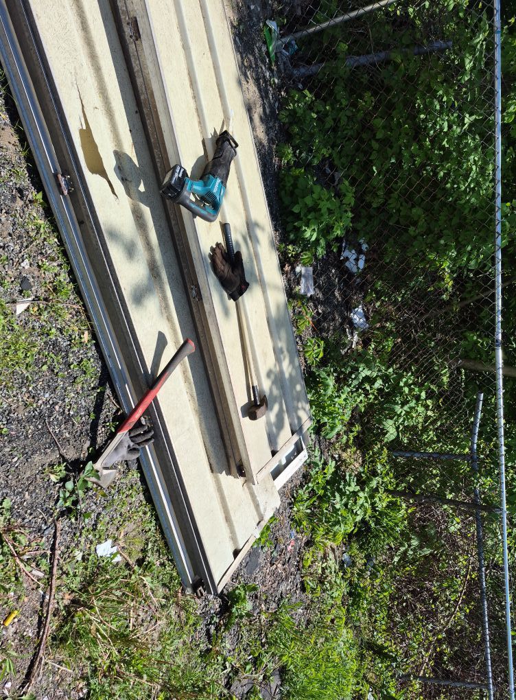 Tools lie on a cream and silver panel; a fence and foliage are in the background.
