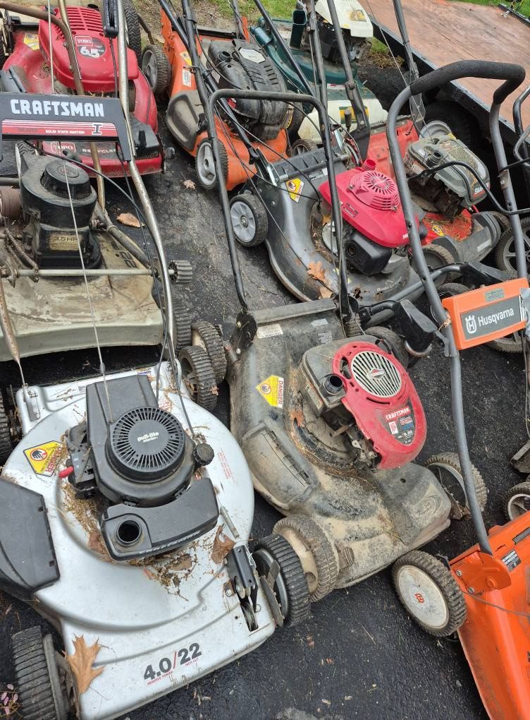 Pile of used lawn mowers, various brands and colors, possibly for sale.